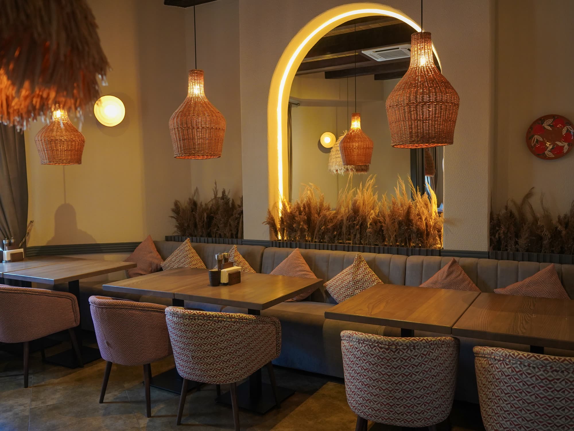 Sala Tbiliso: arcadă luminată, spice uscate, banchetă cu perne kilim și lămpi de răchită